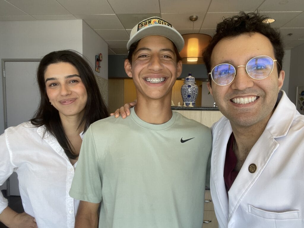 Dr. Shaun Dadjoo poses with two patients, showcasing their smiles in a bright office setting.